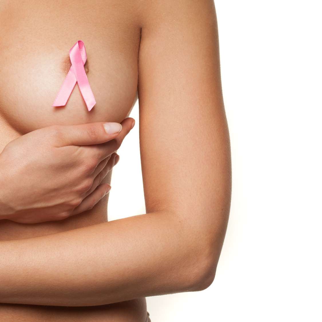 Naked woman wearing a pink breast cancer ribbon attached to her bare nipple as she cups her breast with her hand in a graceful movement, isolated on white